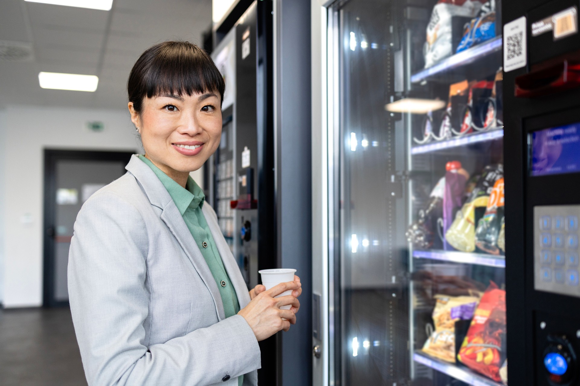 Businesswoman buying coffee and snacks on vending machine on job break.